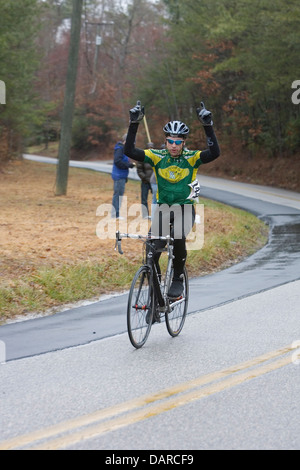 Un maschio ciclista celebra con le braccia in alto dopo aver vinto una gara su strada. Foto Stock