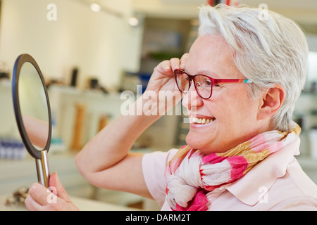 Felice donna anziana con nuovi occhiali guardando in uno specchio a ottico store Foto Stock