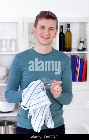 Giovane uomo l'asciugatura e la lucidatura di vetro con un asciugamano da cucina Foto Stock