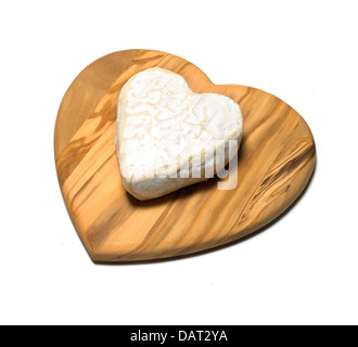 Forma di cuore pezzo di formaggio su un cuore di legno a forma di bordo ritagliato su uno sfondo bianco Foto Stock