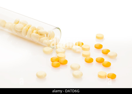 Molti colore trascina in compresse sparsi sul tavolo bianco da laboratorio tubo di prova che raffigura il concetto di farmaco prove e test Foto Stock