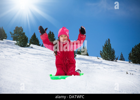 Felice, sorridente ragazza seduta sulla slitta con le mani sollevate sulla slitta nella foresta Foto Stock