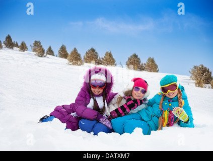 Tre graziosi cercando ragazzi ragazze che stabilisce in snow insieme sulla giornata di sole Foto Stock