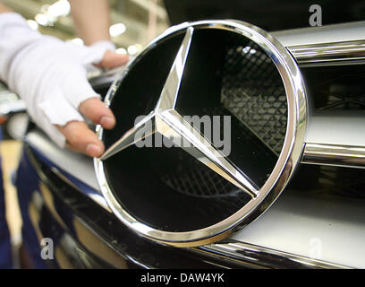 Un dipendente di costruttore DaimlerChrysler AG indossando i guanti di cotone bianco fissa la famosa stella a tre punte con un anello normale Mercedes Benz logo sulla griglia del radiatore di una Mercedes Benz Classe S berlina presso lo stabilimento della società in Sindelfingen, Germania, Venerdì, 02 febbraio 2007. DaimlerChrysler impiega 29,900 persone a livello mondiale la sua più grande impianto di produzione in Sindelfingen, che da Foto Stock