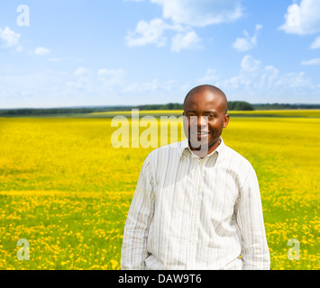 Ritratto di felice nero uomo adulto con un grande sorriso toothy con giallo tarassaco campo sullo sfondo Foto Stock