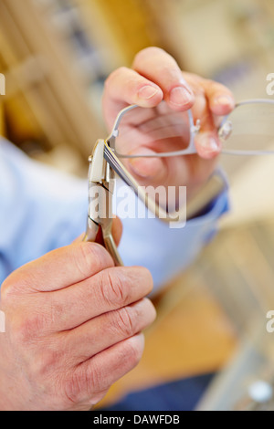 La mano di un ottico con una pinza le riparazioni occhiali Foto Stock