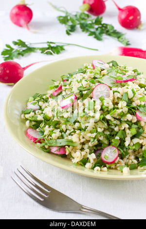 Insalata di bulgur, erbe e verdure con prezzemolo e ravanelli sullo sfondo Foto Stock