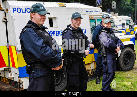 Gli ufficiali di polizia che indossano giubbetti antiproiettile stare accanto a PSNI Landrovers blindati Foto Stock