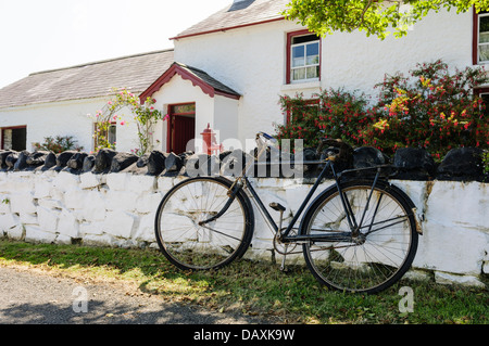 Vecchia bicicletta puntellato contro la parete di un dipinto di bianco agriturismo irlandese Foto Stock