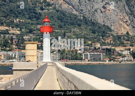 Il bianco e il rosso faro al fine di restringere la passeggiata lungo il mare come case e alberghi sul pendio a Menton, Francia. Foto Stock