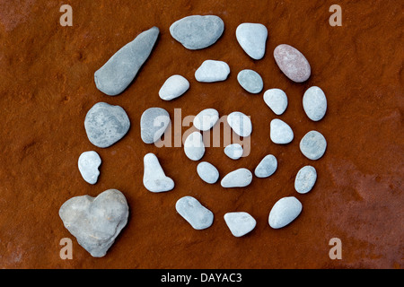 Spirale e cuore pebble su roccia arenaria colorata da depositi di ferro da una metropolitana fonte di acqua Foto Stock