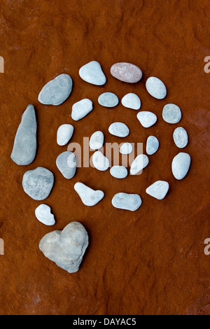 Spirale e cuore pebble su roccia arenaria colorata da depositi di ferro da una metropolitana fonte di acqua Foto Stock