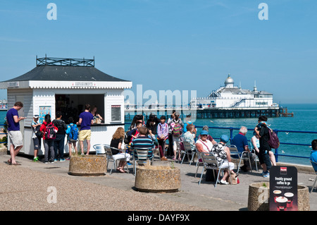 I turisti in un chiosco ristoro sul lungomare di Eastbourne con il molo in background Foto Stock