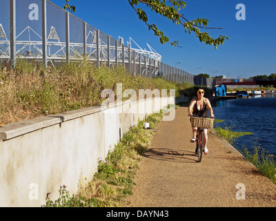 Ciclista femmina lungo il fiume Lea (Lee) Navigazione a Hackney Wick che mostra lo Stadio Olimpico di Stratford Foto Stock