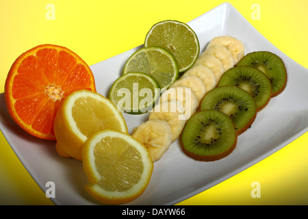 Selezione di frutta su una piastra con sfondo giallo Foto Stock