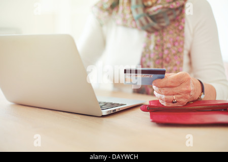 Senior donna la mano in possesso di una carta di credito mentre nella parte anteriore del computer portatile shopping online Foto Stock