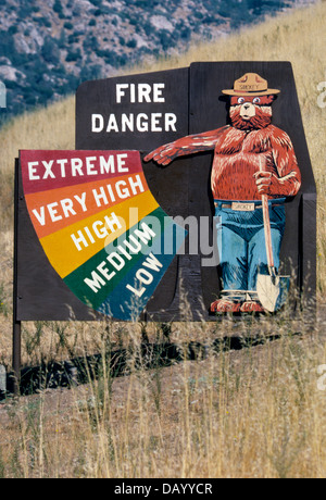 Un'icona americana in una campagna di prevenzione di incendi, Smokey Bear punti di estremo pericolo di incendio su un segno esterno nel mezzo di erbe secche in California, Stati Uniti d'America. Foto Stock