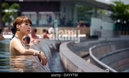 Bella turista giapponese che soggiornano presso il Marina Bay Sands in ammollo nella piscina infinity e godendo di Singapore il paesaggio urbano Foto Stock
