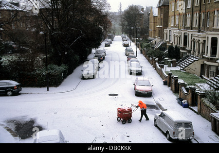 Portalettere consegna post con un carrello in una suburban London street in inverno, Inghilterra Foto Stock
