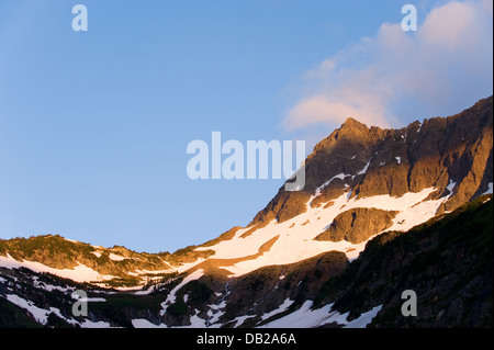 Il sole al tramonto proietta una luce calda sulle montagne sopra la cascata passano a Washington North Cascades. Foto Stock