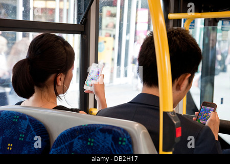 Due persone sedute su un Bus londinese giocando Candy Crush Saga sul loro iphone, Londra, Inghilterra Foto Stock