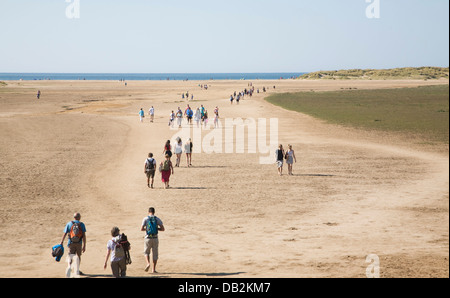 Persone che camminano verso il mare attraverso ampia spiaggia sabbiosa Holkham Norfolk Inghilterra Foto Stock