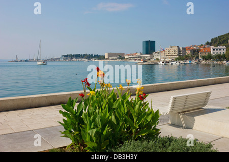 Vista panoramica del lungomare di Riva in Split, Croazia con fiori colorati, una panca e barche a vela in marina. Foto Stock