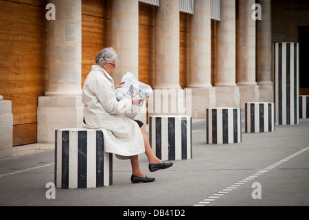 Donna che legge il giornale mentre è seduto su una colonna nel cortile del Palais Royal, Paris Francia Foto Stock