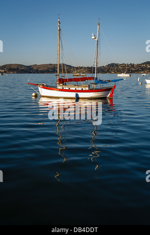 Graziosa barca a vela rossa e bianca ormeggiata in un porto tranquillo all'alba Foto Stock