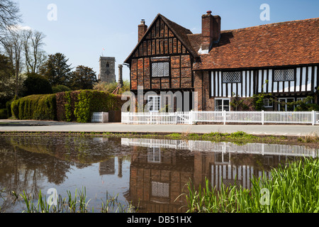 In mattoni e legno a casa accanto al villaggio Duck Pond con uno scorcio di una chiesa al di là, Aldbury, Hertfordshire, Inghilterra Foto Stock