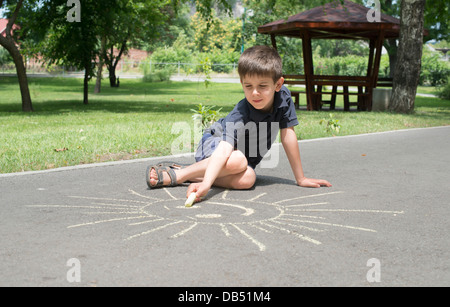 Bambino disegno sun su asfalto in un parco Foto Stock