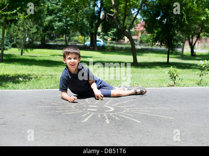 Bambino disegno sun su asfalto in un parco Foto Stock