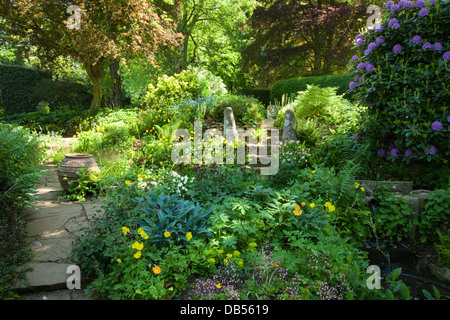 Una vista colorata dall'interno del giardino d'acqua dei giardini di Coton Manor che discende dolcemente dal giardino boschivo, Northamptonshire, Inghilterra. Foto Stock