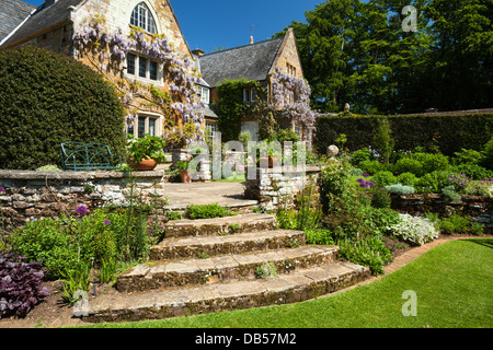 Gradini in pietra conducono ad una terrazza giardino con fioritura di arrampicata di glicine le pareti di pietra di Coton Manor al di là, Northamptonshire, Inghilterra Foto Stock