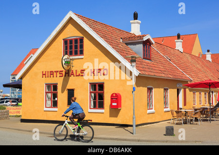 Donna in bicicletta su una bicicletta passato famosa Hirtshals Kro pub e adiacente hotel nella città di Hirtshals, Nord dello Jutland, Danimarca Foto Stock