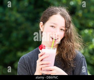 Foto della ragazza giovane prepara a bere un frullato fragole all'aperto con uscita sfocata luminose verdi alberi in background Foto Stock