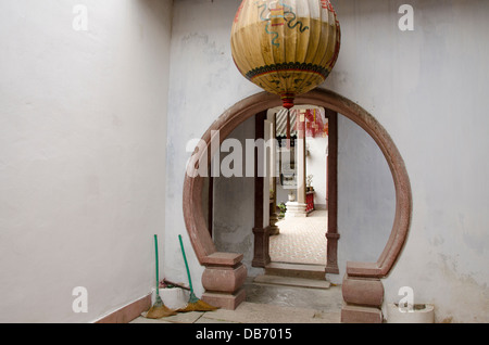 Il Vietnam, Hoi An. Assembly Hall del Cinese Cantonese Congregazione. Stile cinese round porta con la lanterna e ginestre. Foto Stock