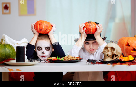 Foto di twin eerie boys holding zucche di Halloween sopra le loro teste e guardando la fotocamera Foto Stock