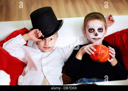 Foto di due eerie ragazzi guardando la fotocamera mentre vi rilassate sul divano sul giorno di Halloween Foto Stock