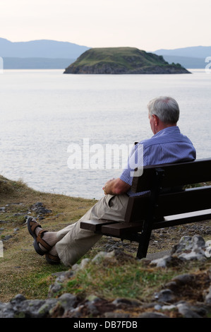 Un uomo seduto sulla panca in legno all'esterno. Foto Stock