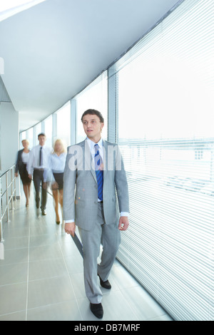 Ritratto di imprenditore fiducioso a camminare lungo il corridoio con il team di partner sullo sfondo Foto Stock