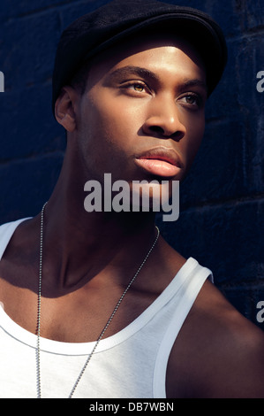 Bel giovane attraente african american uomo che indossa un cappello ritratto cercando la faccia sinistra illuminata dalla luce del sole gli occhi pieni di emozione Foto Stock