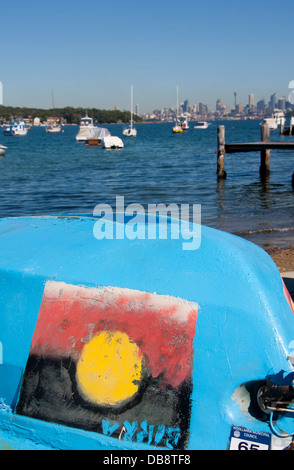 Watsons barca sulla spiaggia con bandiera aborigena dipinta sul lato dello skyline della città in distanza Sydney New South Wales (NSW) Australia Foto Stock