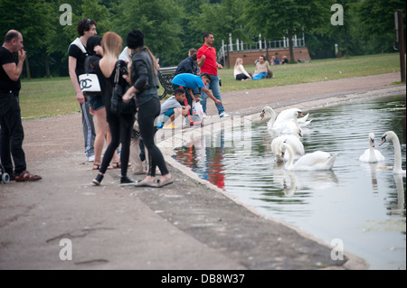 Multi culturale di alimentazione persone cigni al laghetto in Kensington Gardens mescolati gruppi di età e sesso Foto Stock