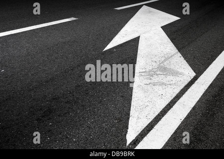 La segnaletica stradale con righe bianche e freccia su asfalto scuro Foto Stock