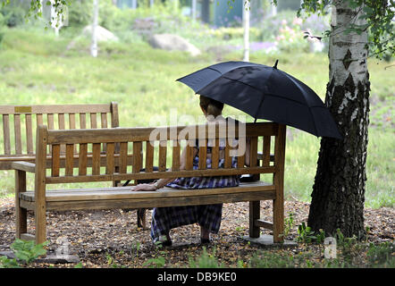 Una donna si siede sotto un ombrello per proteggersi contro il sole su una calda giornata al Parco di rododendro in Bremen, Germania, 26 luglio 2013. Foto: INGO WAGNER Foto Stock