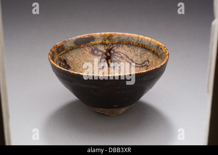 Questa ciotola da tè (chawan) è decorata con spray floreali e foenici, simboleggiando il rinnovamento e la prosperità. Il suo design delicato, i raffinati smalti e la raffinata forma riflettono l'abilità artistica della ceramica giapponese, enfatizzando sia il valore estetico che simbolico nella cultura del tè. Foto Stock