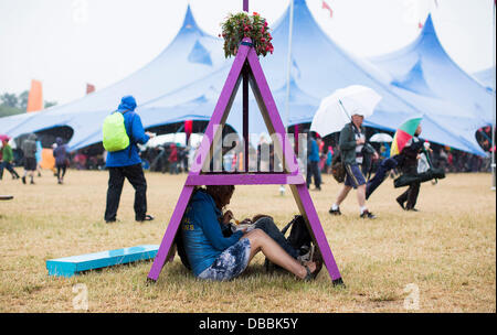 Malmesbury, Wiltshire, Regno Unito. 27 Luglio, 2013. Persone riparo sotto un segno dalla pioggia DEL FESTIVAL WOMAD in Charlton Park vicino a Malmesbury nel Wiltshire. Il world music festival attira quasi 40.000 persone alla posizione rurale. 27 luglio 2013 Credit: Adam Gasson/Alamy Live News Foto Stock