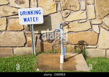 Acqua potabile tocca con segno e acqua in marcia dietro un muro di pietra Foto Stock