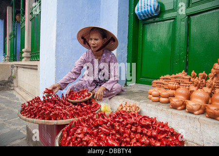 La donna nel cappello conico di vendita fischietti in ceramica sulla strada di Hoi An, Vietnam, sud-est asiatico Foto Stock